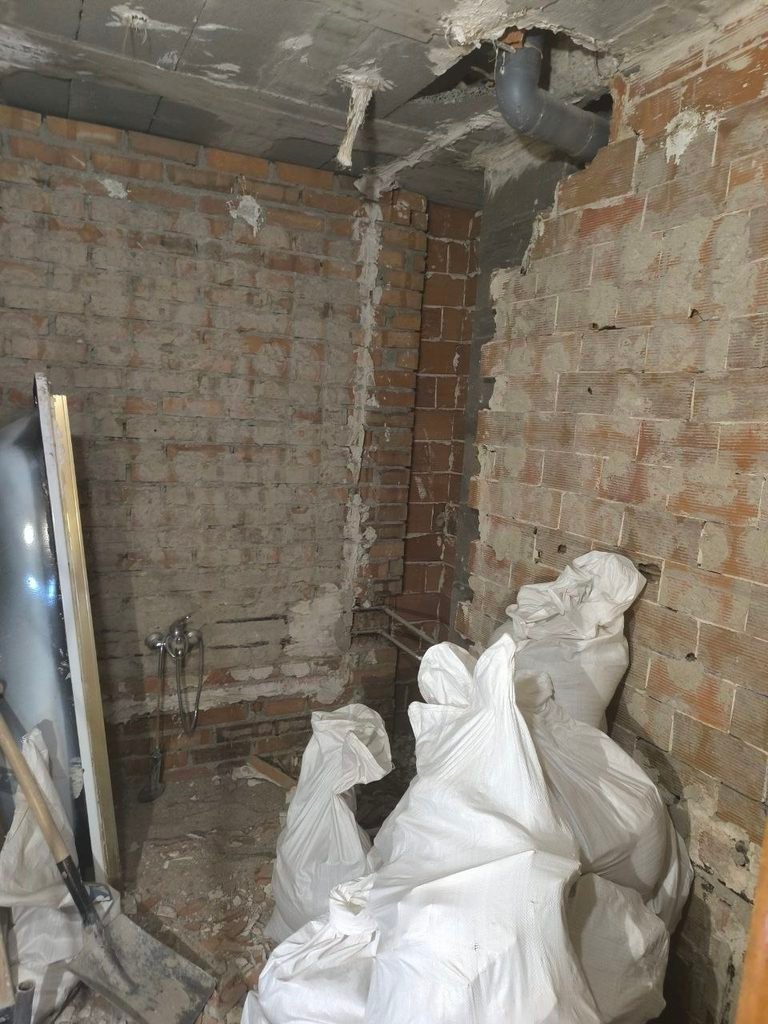 Baño en fase de demolición con paredes de ladrillo y retirada de escombros en Coslada